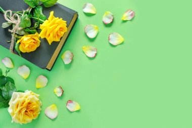 Güzel bir buket sarı gül, eski bir kitap ve yeşil masanın üzerinde çiçek yaprakları. Tatil davetiyesi için ofis ve bir sayfa kağıt. Ya da tebrikler.