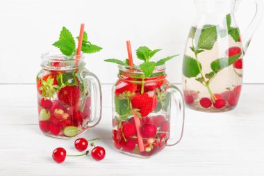 Taze taze meyve suyu, çilek, frenk üzümü ve Bektaşi üzümü beyaz ahşap masada.