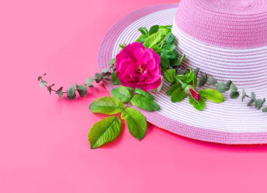 Güneşli bir günde gül buketi ve okaliptüslü güzel bir hasır şapka. Doğanın pembe kağıt arka planı.