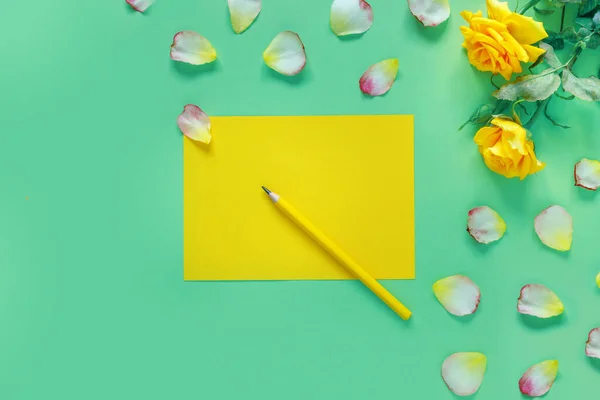 緑のテーブルの上に黄色のバラと花の花びらの美しい花束 テキスト用のノートと鉛筆 — ストック写真
