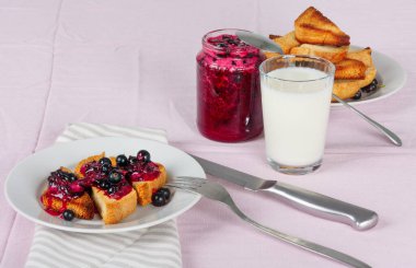 Lezzetli tost ekmeği ev yapımı frenk üzümü reçeli ve parlak kırmızı masa örtüsü üzerinde süt.