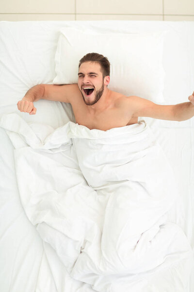 top view. happy man waking up in a comfortable bed
