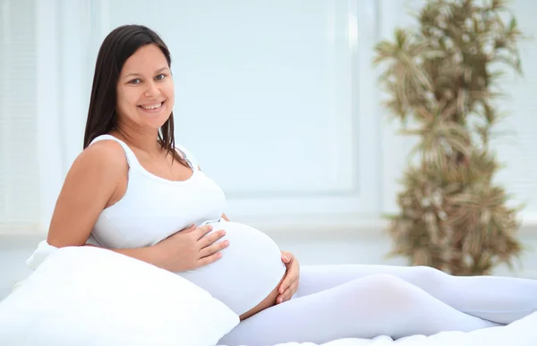 Mulher grávida bonita sentada no sofá e mantendo a mão na barriga . — Fotografia de Stock