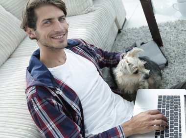 yakışıklı adam köpeğini sarılma ve kanepede oturan dizüstü bilgisayar ile