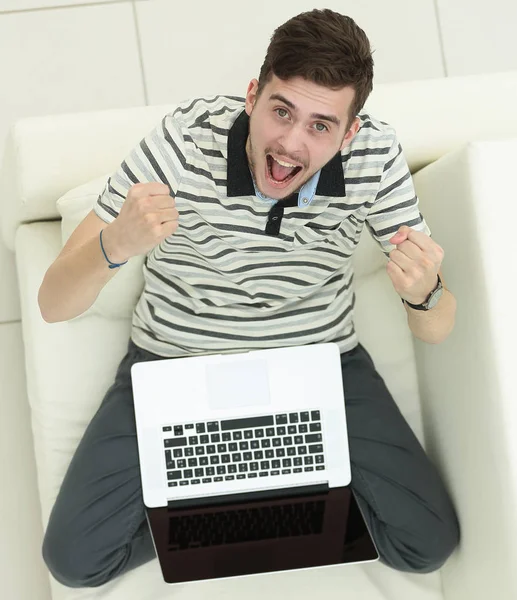 Vue du haut. jubilant jeune homme avec ordinateur portable assis sur le canapé — Photo