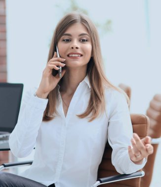 Ofiste oturan iş kadını cep telefonuyla konuşuyor.