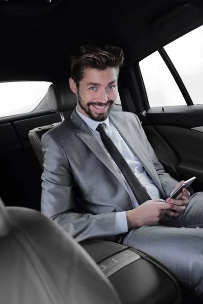 Людина в костюмі сидить в машині і читає повідомлення на смартфоні — стокове фото