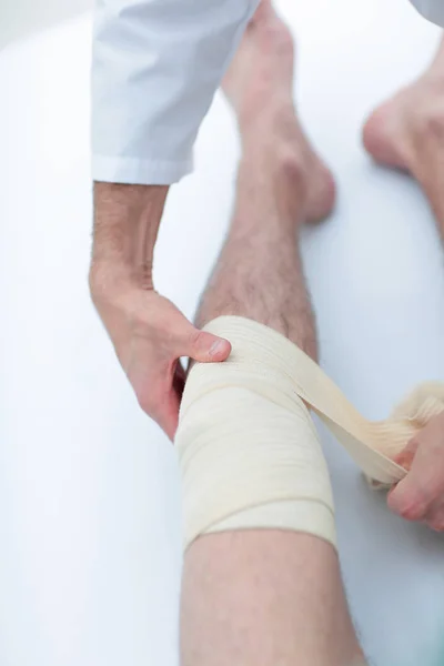 Nahaufnahme. Arzt bandagiert ein Bein des Patienten — Stockfoto
