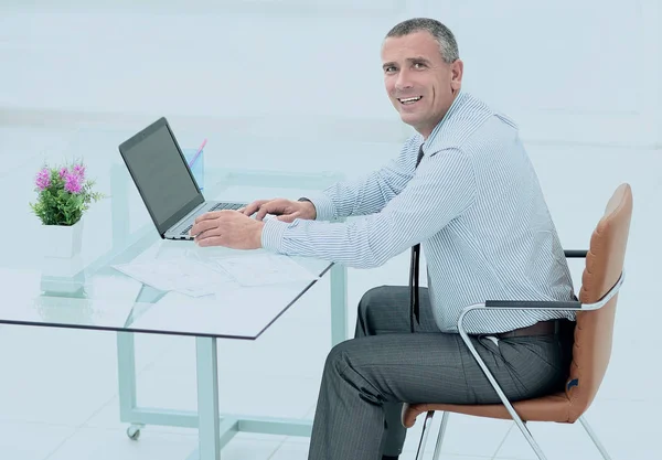 Portret van een lachende rijpe zakenman achter het bureau zit — Stockfoto