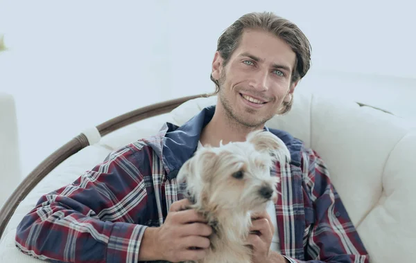 Primer plano de un chico sonriente acariciando a su perro mientras está sentado en un sillón grande . —  Fotos de Stock