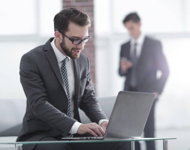 Yakışıklı iş adamı ofiste dizüstü bilgisayarla çalışıyor.