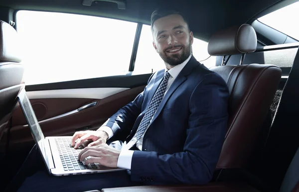 Uomo d'affari con computer portatile seduto sul sedile posteriore di una macchina — Foto Stock