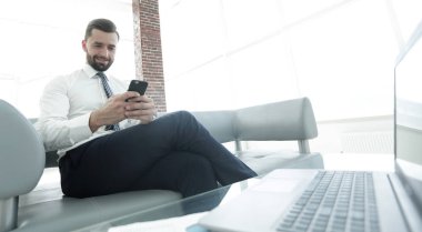 İşadamı ile modern bir ofis lobisinde oturan bir smartphone