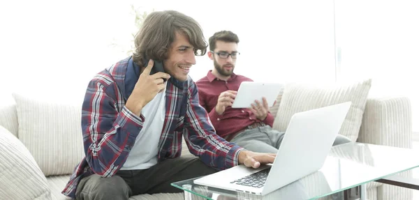 Dois caras sentados no sofá, falando em um telefone celular e conversando na Internet . — Fotografia de Stock