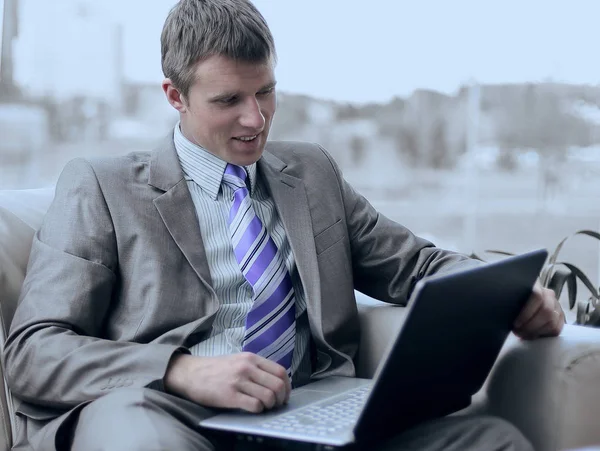 Молодой бизнесмен сидит в офисном холле и работает с ноутбуком — стоковое фото
