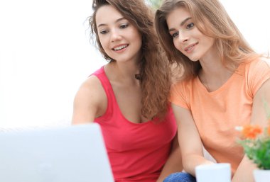 iki öğrenci kız kanepede otururken dizüstü bilgisayar ekranına bakarak.