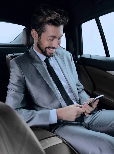 Muž v obleku, sedí v autě a čtení zpráv na smartphone — Stock fotografie