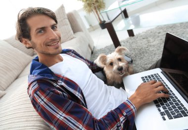 yakışıklı adam köpeğini sarılma ve kanepede oturan dizüstü bilgisayar ile