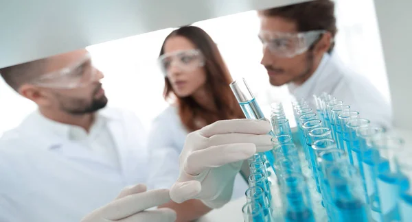 Background image is a group of scientists studying the liquid in the glass tube. — Stock Photo, Image