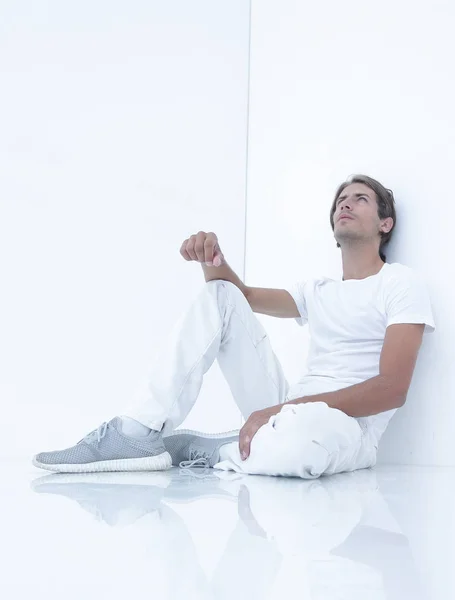 Jovem sonhador sentado ao lado de uma parede branca . — Fotografia de Stock