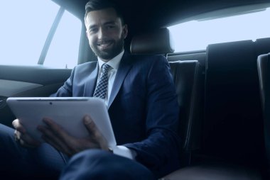 bir arabanın arka koltuğunda çalışma ve bir tablet kullanarak iş adamı