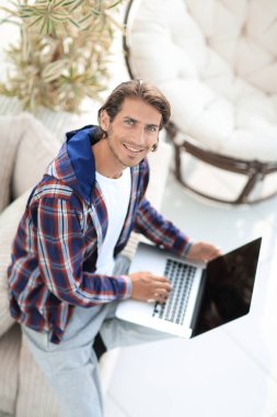 dizüstü bilgisayarda çalışan ve kameraya bakarak bir genç adam. Yukarıdan görüntülemek