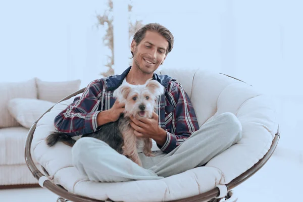 Schöner Kerl mit Hund sitzt in einem großen Sessel. — Stockfoto