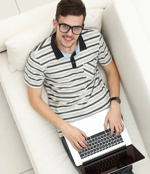 Homem moderno trabalha em um laptop sentado no sofá — Fotografia de Stock