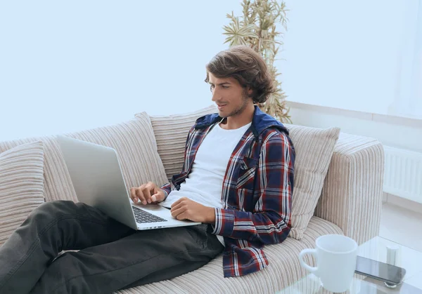 Młody mężczyzna pracujący na laptopie siedząc na kanapie — Zdjęcie stockowe