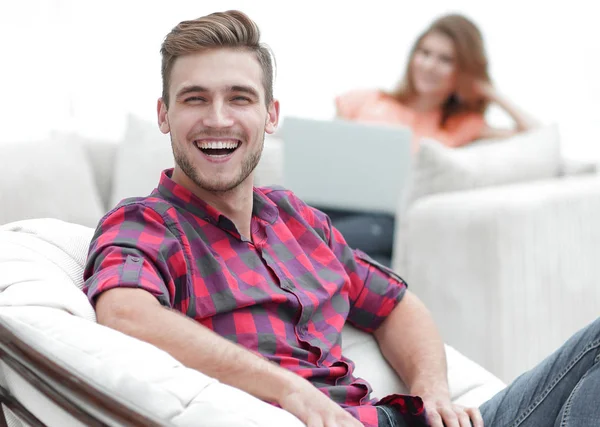 Bulanık arka planda büyük bir sandalyede oturan mutlu genç adam.