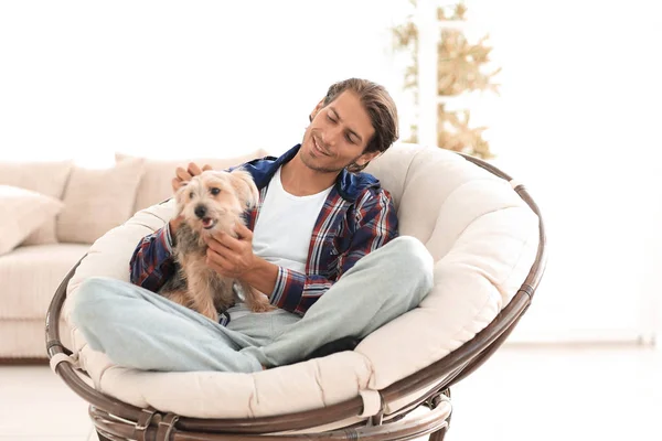 Schöner Kerl mit Hund sitzt in einem großen Sessel. — Stockfoto