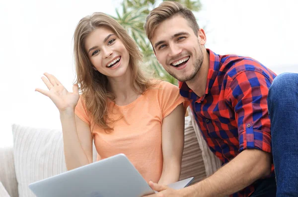 Feliz pareja riendo, sentado en el sofá delante de la computadora portátil abierta — Foto de Stock
