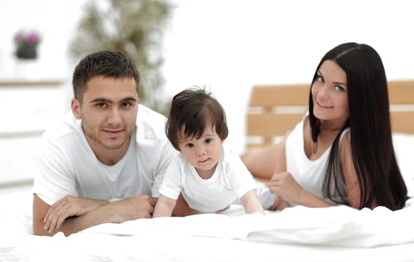 Portrait of happy young family lying in bed together — Stock Photo, Image