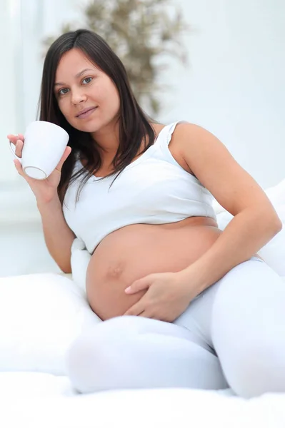 リビング ルームに座っている牛乳を飲んで幸せな妊娠中の女性. — ストック写真