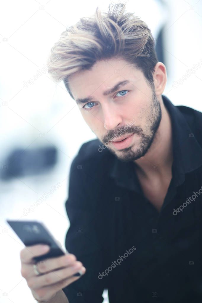 A stylish bearded male sits and uses a smartphone.