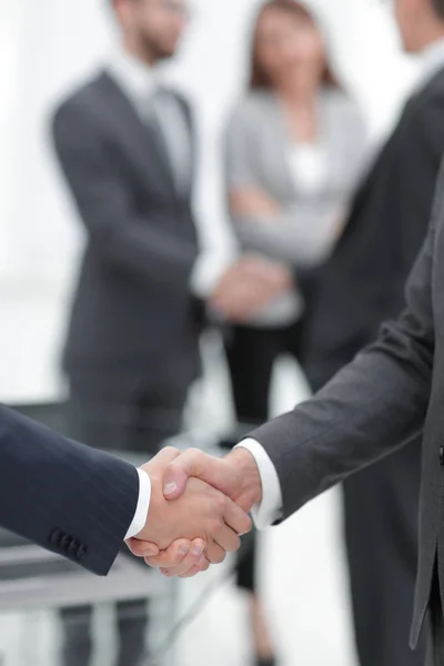 Dos hombres de negocios estrechando la mano con sus colegas de fondo. — Foto de Stock