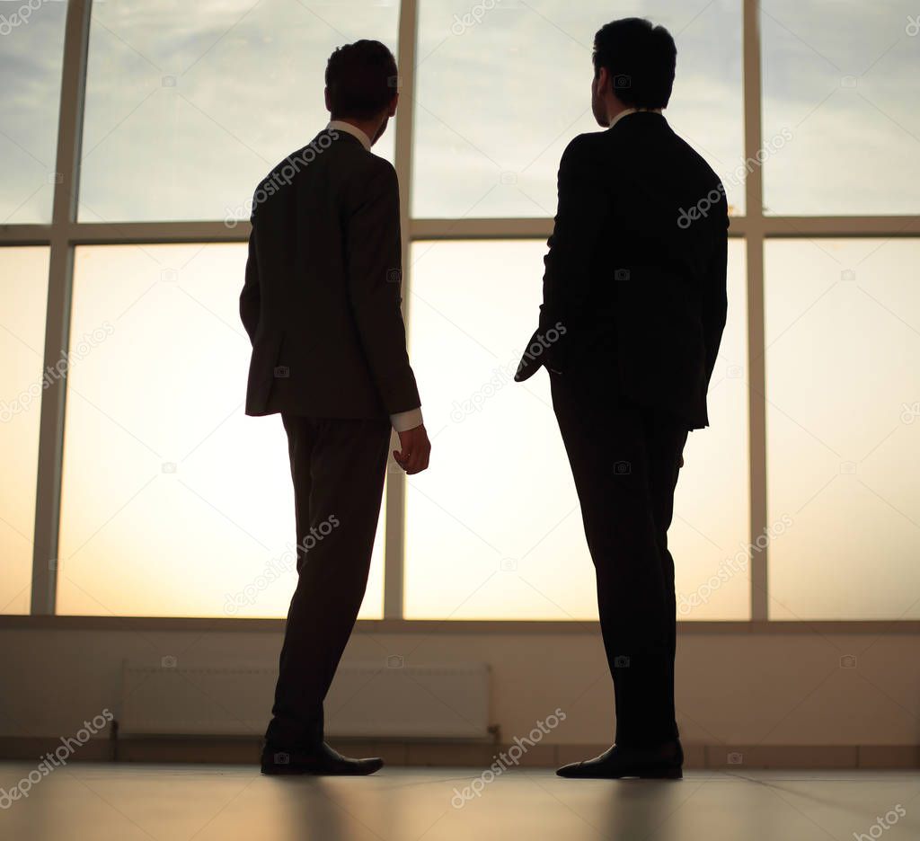 two businessmen look at the city from the window of the business center