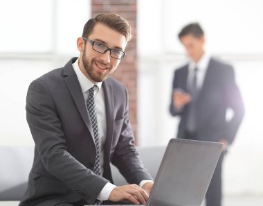 Yakışıklı iş adamı ofiste dizüstü bilgisayarla çalışıyor.