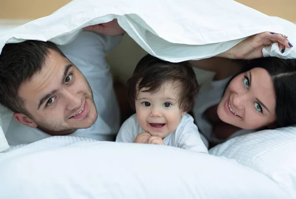 Happy family posing under a duvet while looking at the camera — Stock Photo, Image