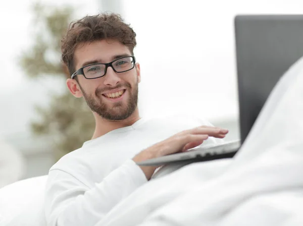 Homme souriant en utilisant un ordinateur portable couché sur le lit — Photo