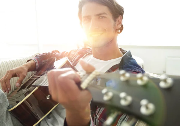 Jongen met gitaar die zittend op de Bank in de woonkamer. concept van een levensstijl — Stockfoto