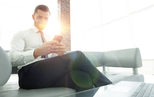 Empresário com um smartphone sentado no lobby de um escritório moderno — Fotografia de Stock