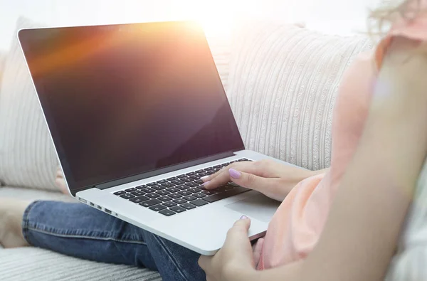 Молода жінка працює з ноутбуком, сидячи на дивані — стокове фото