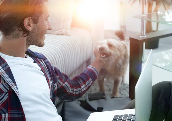 Stijlvolle jongeman streelde zijn huisdier en bezig met laptop — Stockfoto