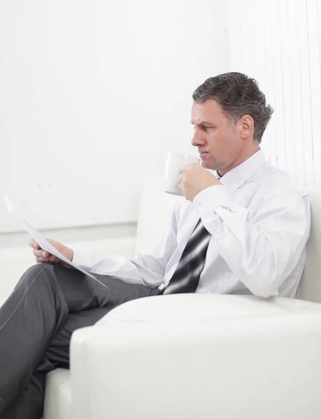 Affärsman som läser ett dokument medan du sitter i en stol på hotellrummet. — Stockfoto