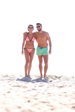 Genç çift el ele tutuşup kumsalda yürüyor..