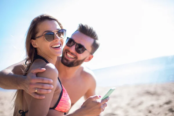 Romantisches Paar beim Stöbern seiner Fotos am Strand — Stockfoto