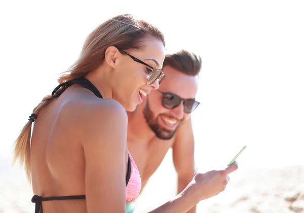 Casal sorridente navegando suas fotos na praia — Fotografia de Stock