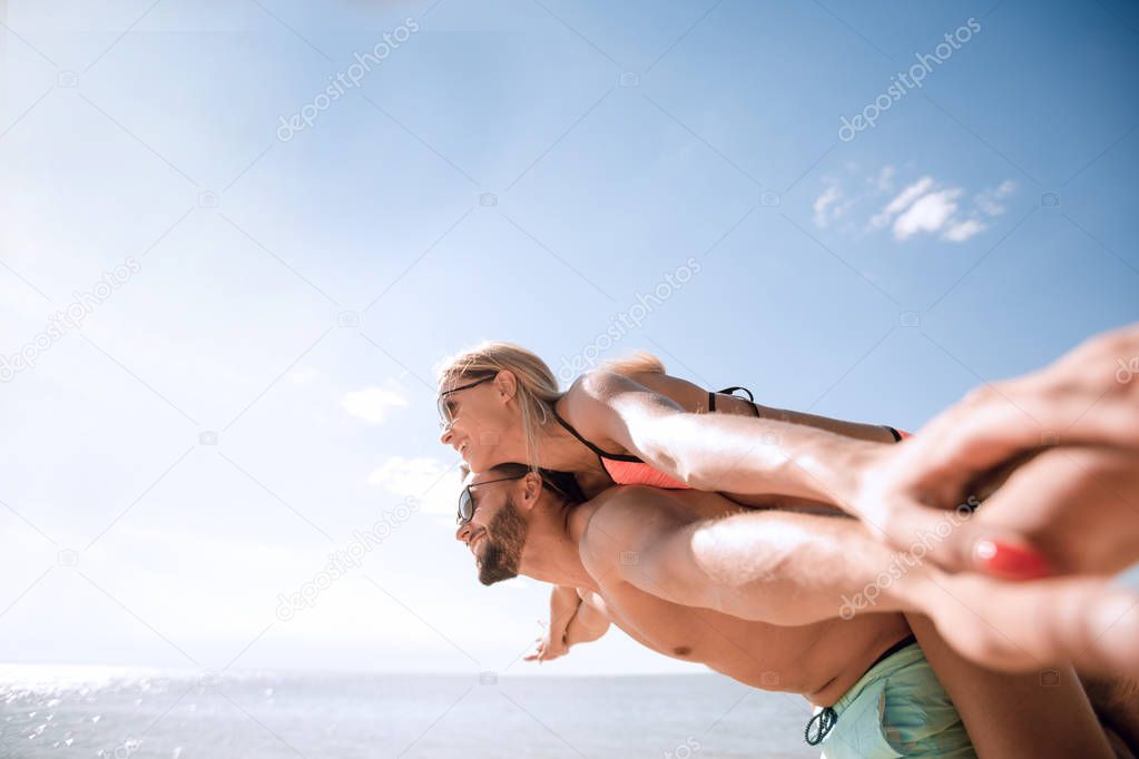 Man carrying woman piggyback on beach.
