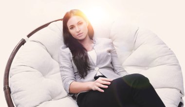 Yuvarlak, yumuşak bir sandalyede oturan modern genç kadın.